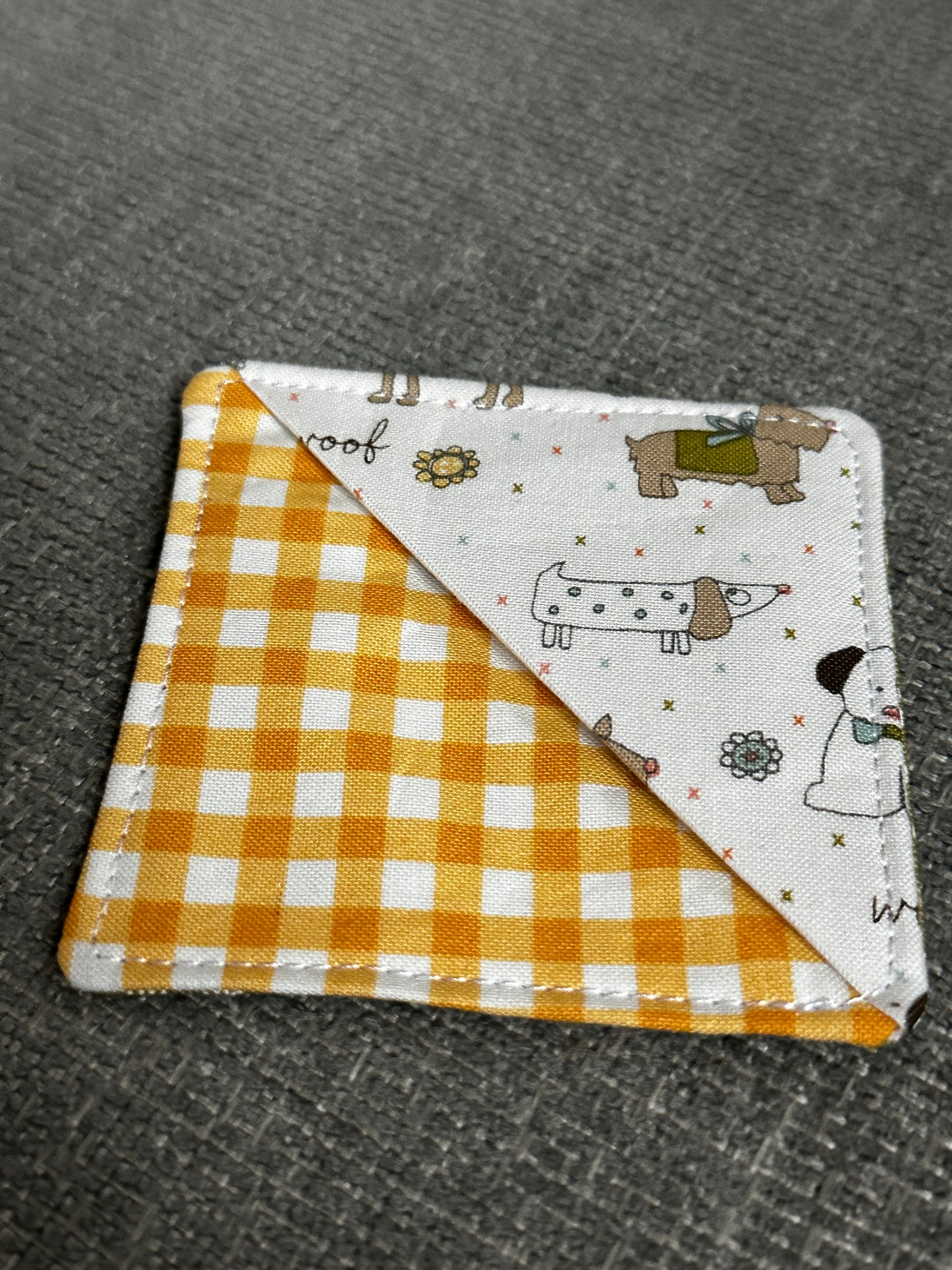 Fabric patch with cartoon characters on one side and yellow checkered pattern on the other, on a textured gray background.