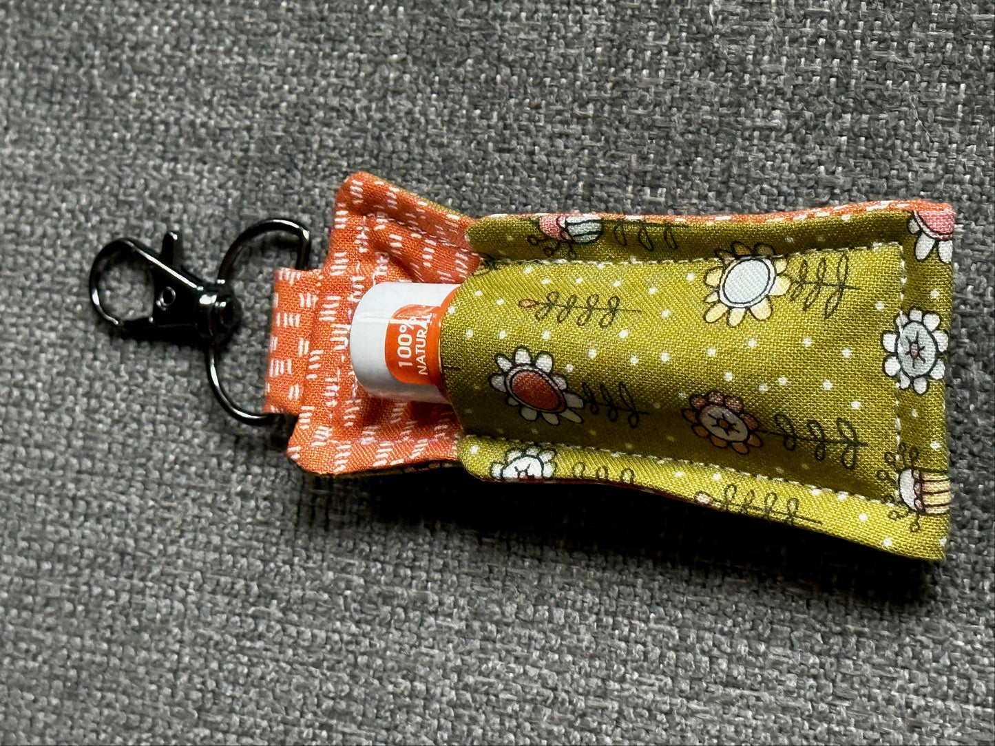 Small green pouch with floral patterns and a keychain clip on a gray background